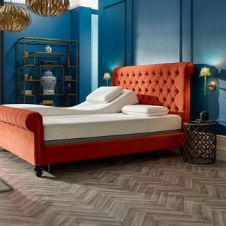 Wide view of the Opera Dalta Adjustable Bed set in a bedroom with blue painted walls. The bed is in a burnt orange fabric. A Sleigh style bed with a high button back headboard.