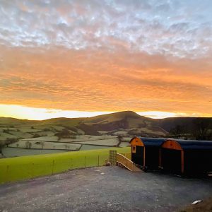 Hafan y Mynydd - Accessible Shepherds Hut in Rural Wales - image shows the hut at sunset with orangey yellow skies above the mountains in the distance