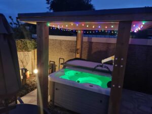 Image of the hot tub at Crescent Hideaway, Weston Super Mare at night with a green light on in the tub. The accompanying hoist allows people with complex needs to experience this luxury
