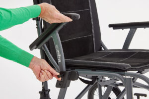 A lady's hands are flipping up the armrest on the Magnelite Transit Wheelchair to enable a smooth side transfer