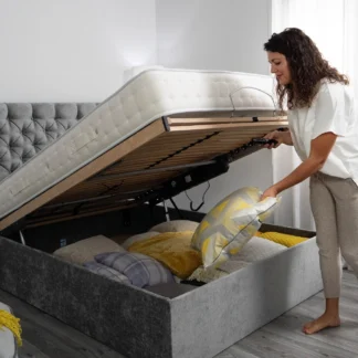Varimatic Ottoman Adjustable Bed - Bed is raised to reveal the ottoman storage within and a lady is stood at the foot of the bed, stowing a cushion into it.